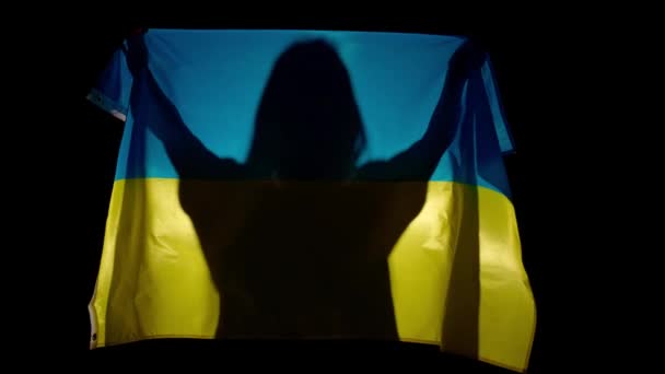 国旗愛国的な広告コンセプト 黒い背景に対して大きな旗を掲げるシルエット 手に持っているウクライナの国旗を持つ女性のシルエット — ストック動画