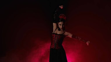 Modern koreografi bir dans. Kırmızı ışık ve dumanla siyah arka planda dans eden kadın. Kırmızı ve siyah elbiseli İspanyol dansçı flamenko koreografisinin unsurlarını gösteriyor.