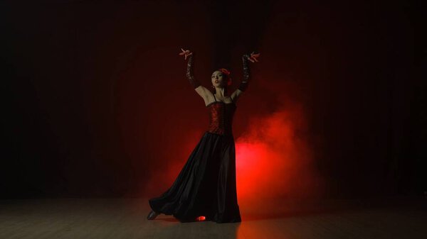Modern choreography an dance. Woman dancing on black background with red light and smoke. Spanish dancer in red and black dress demonstrates elements of flamenco choreography.