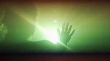 Işık konseptinde siluet. Stüdyoda siyah dumanlı arka planda parlak renkli ışığa karşı kadın modeli. Elleri ışık huzmelerinde yürüyen bir kadının silüeti.