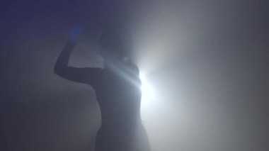 Işık konseptinde siluet. Stüdyoda siyah arka planda parlak ışığa karşı kadın modeli. Kadın silueti hareket eden bir el Karanlıkta ışık ışınıyla oynuyor.