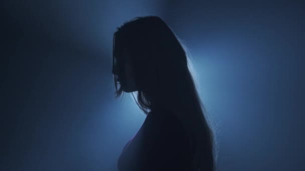 照明コンセプトのシルエット スタジオの黒いスモーキーな背景の明るい光に対する女性モデル 暗闇に光の光に囲まれた女性のシルエット サイドビュー — ストック動画