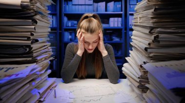 Sıkı çalışma konsepti. Yorgun, genç bir iş kadını ofis çalışanı gece geç saatlere kadar evrak işleriyle meşgul. Kadın çok üzgün ve kızgın..