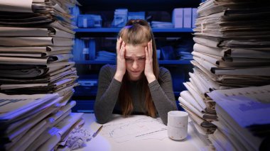 Sıkı çalışma konsepti. Yorgun, genç bir iş kadını ofis çalışanı gece geç saatlere kadar evrak işleriyle meşgul. Kadın belgeleri okuyor. Stresli, sinirli, depresif ifade..
