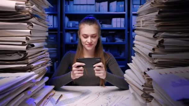 ハードワークコンセプト 夜遅く勤務するデスクで働く若いビジネス女性事務所の従業員は 書類の仕事に過負荷を被りました 女性はスマートフォンでゲームをプレイし 先延ばし作業 — ストック動画