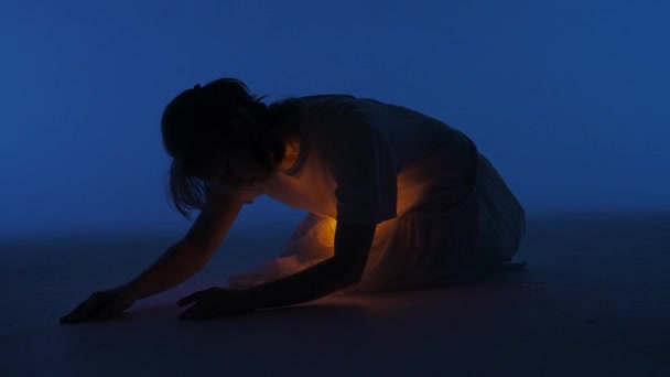 当代实验舞蹈概念 在演播室里表演的女舞蹈演员 年轻的女人躺在黑暗的工作室里 衬衫下面的箱子里闪烁着温暖的光芒 全速60发 — 图库视频影像