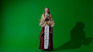 Tarihsel kişi modern yaşam tarzı reklamı. Krom anahtar yeşil ekran arka planında eski giysili bir kadın. Rönesans tarzı elbiseli kadın para hayranı ve çok mutlu..