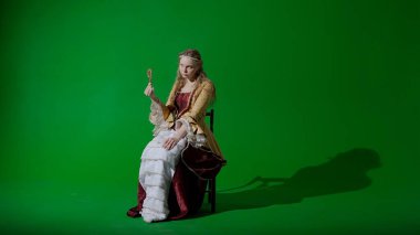 Tarihsel kişi modern yaşam tarzı reklamı. Krom anahtar yeşil ekran arka planında eski giysili bir kadın. Rönesans tarzı elbiseli bir kadın elinde şeker kamışı ile oturmuş şekerleme yiyor.