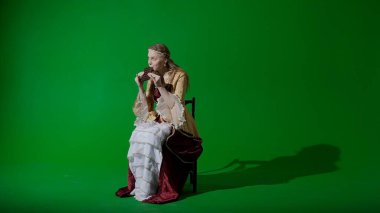 Tarihsel kişi modern yaşam tarzı reklamı. Krom anahtar yeşil ekran arka planında eski giysili bir kadın. Rönesans tarzı elbise giymiş bir kadın elinde çikolatayla oturmuş, şeker yiyor..