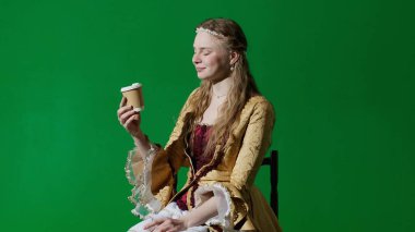 Tarihsel kişi modern yaşam tarzı reklamı. Krom anahtar yeşil ekran arka planında eski giysili bir kadın. Rönesans elbisesi giymiş, kahve içen, kağıt belgelerle çalışan bir iş kadını..