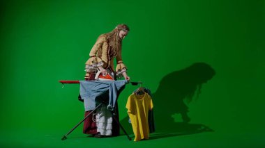 Tarihsel kişi modern yaşam tarzı reklamı. Krom anahtar yeşil ekran arka planında eski giysili bir kadın. Rönesans tarzı elbiseli bir kadın çamaşırları ütülüyor..