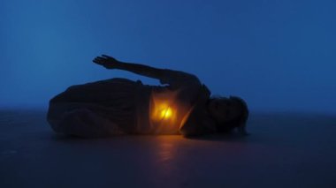 Çağdaş deneysel koreografi konsepti. Stüdyoda kadın dansçı sahne alıyor. Genç bir kadın karanlık stüdyoda yatıyor ve göğsünün altında sıcak bir ışık parlıyor. Tam vuruş 60 fps