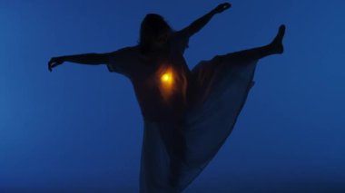 Çağdaş deneysel koreografi konsepti. Stüdyoda kadın dansçı sahne alıyor. Karanlık stüdyoda dans eden genç bir kadın. Gömleğinin altında sıcak bir ışık parlıyor. Tam vuruş 30 fps.