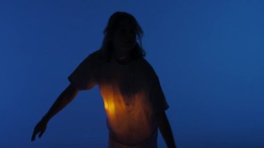 Çağdaş deneysel koreografi konsepti. Stüdyoda kadın dansçı sahne alıyor. Karanlık stüdyoda dans eden genç bir kadın. Gömleğinin altında sıcak bir ışık parlıyor. 30 fps