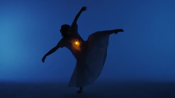 当代实验舞蹈概念 在演播室里表演的女舞蹈演员 年轻女子在黑暗的演播室里跳舞 衬衫下面的胸膛里闪烁着温暖的光芒 全速30发 — 图库视频影像