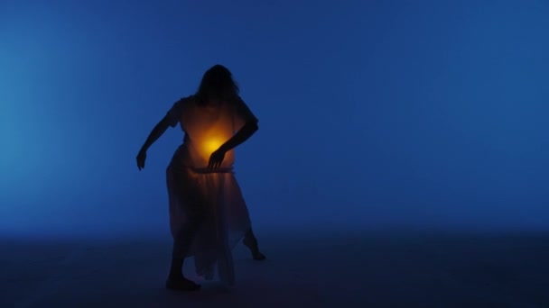 当代实验舞蹈概念 在演播室里表演的女舞蹈演员 年轻女子在黑暗的演播室里跳舞 衬衫下面的胸膛里闪烁着温暖的光芒 全速30发 — 图库视频影像