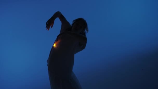 当代实验舞蹈概念 在演播室里表演的女舞蹈演员 年轻女子在黑暗的演播室里跳舞 衬衫下面的胸膛里闪烁着温暖的光芒 Fps — 图库视频影像