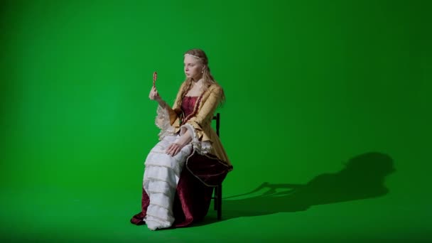 歴史的人物現代ライフスタイル広告 クロマキーの緑色の背景に古代の服を着た女性 ルネッサンススタイルのドレスで女性が楽しむお菓子を食べるキャンディーケインを保持している — ストック動画
