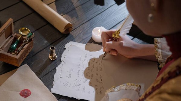 Historical letter creative concept. Female in antique outfit writes with feather pen. Over shoulder shot of woman writing a letter with vintage quill feather pen on old parchment paper at the desk.