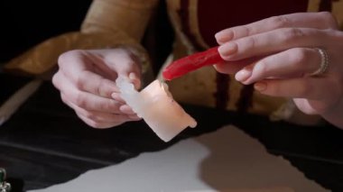 Eski bir harf yaratıcı kavramı. Mumlu, antika kostümlü bir kadın. Rönesans elbisesi giymiş bir kadın elinde balmumu çubuğuyla onu bir mum ateşinde ısıtır, kağıda düşen balmumu damlaları..