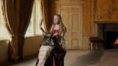 Tarihsel kişi modern yaşam tarzı reklamı. Tarihi iç mekanın arka planında, kadim kıyafetli bir kadın. Rönesans elbisesi giymiş bir kadın çöp torbası tutuyor ve içine bakıyor..