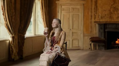 Tarihsel kişi modern yaşam tarzı reklamı. Tarihi iç mekanın arka planında, kadim kıyafetli bir kadın. Rönesans tarzı elbiseli bir kadın oturmuş kağıt bardaktan kahve içiyor..