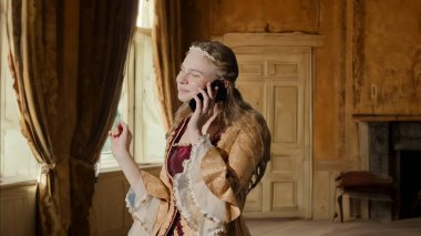 Tarihsel kişi modern yaşam tarzı reklamı. Tarihi iç mekanın arka planında, kadim kıyafetli bir kadın. Rönesans tarzı elbiseli bir kadın akıllı telefondan arıyor..