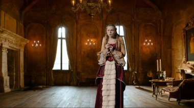 Tarihsel kişi modern yaşam tarzı reklamı. Tarihi iç mekanın arka planında, kadim kıyafetli bir kadın. Rönesans tarzı elbiseli bir kadın kameraya bakıyor, korkmuş bir surat..