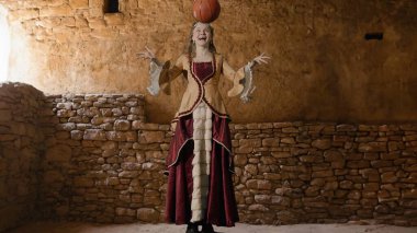 Tarihsel kişi modern yaşam tarzı reklamı. Tarihi iç mekanın arka planında, kadim kıyafetli bir kadın. Rönesans tarzı elbiseli kadın basketbol topu atıyor..