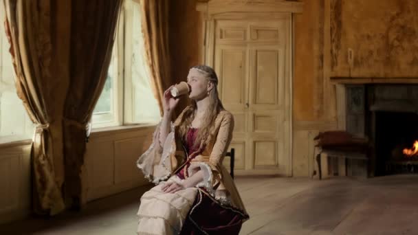 历史人物现代生活方式广告 穿着古装的女人 背景是历史的内部 身着文艺复兴风格服装的女性坐着用纸杯喝咖啡 — 图库视频影像