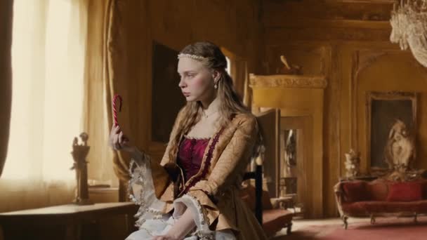 历史人物现代生活方式广告 穿着古装的女人 背景是历史的内部 穿着复兴风格的女性坐在那里拿着甘蔗 吃着糖果 享受着 — 图库视频影像