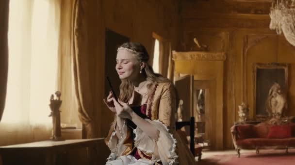 历史人物现代生活方式广告 穿着古装的女人 背景是历史的内部 身着文艺复兴风格服装的女性坐在那里拿着巧克力棒 吃着糖果 — 图库视频影像