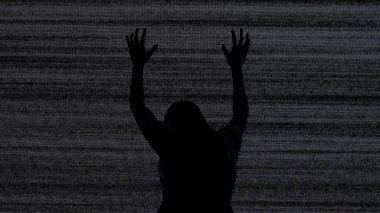 Cadılar Bayramı korku filmi yaratıcı konsepti. Siluet dijital televizyon ekranına karşı. Gerilim sahnesi korkmuş kadın silueti yerde oturmuş gürültüyle büyük dijital ekrana çarpıyor..