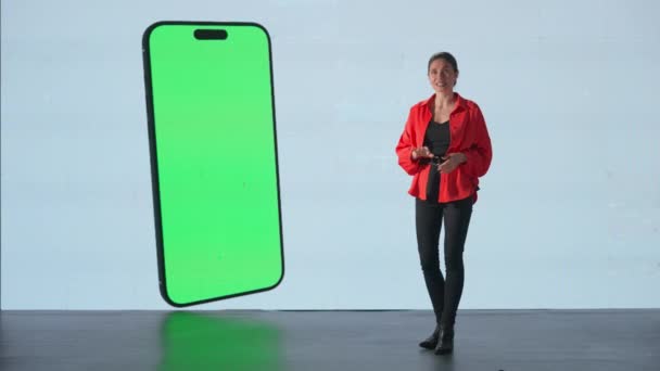 商务会议演讲 会议期间 妇女在舞台上介绍项目 赛欧女演说家介绍产品 智能手机彩色键绿色屏幕展示在一个巨大的Led屏幕上 — 图库视频影像