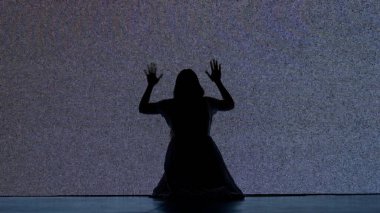 Cadılar Bayramı korku filmi yaratıcı konsepti. Siluet dijital televizyon ekranına karşı. Gerilim sahnesi korkmuş kadın silueti yerde oturmuş gürültüyle büyük dijital ekrana çarpıyor..