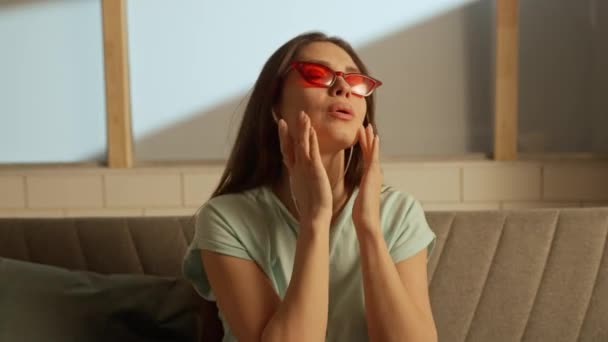 音楽と人間の感情クリエイティブ広告コンセプト ソファーに座っている部屋の若者の肖像画 ソファーの赤い眼鏡とイヤホンの女性は音楽を聞き 歌に詰め込む — ストック動画
