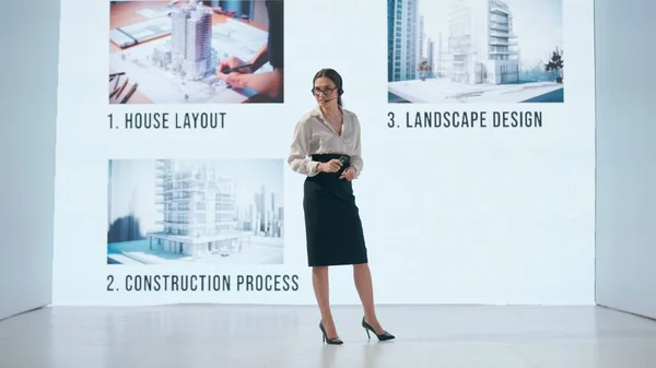 ビジネスウーマンは 彼女の背後にある大きなディスプレイに示されたマルチフェーズアーキテクチャプロジェクトを提示し レイアウトから最終的なデザインまでのステージを詳述しています — ストック写真