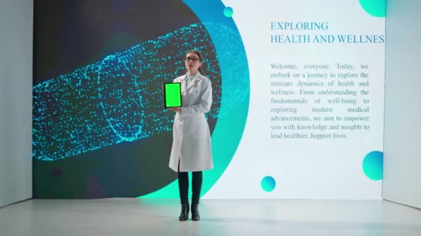 一位身穿白衣的妇女站在一个巨大的数字屏幕上的药品前 一位女科学家展示了带有绿色屏风的平板电脑 并发表了科学性演讲 — 图库视频影像