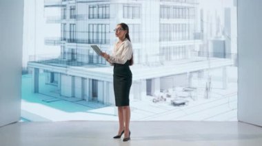 Bir kadın, çok katlı bir binanın holografik projeksiyonuyla etkileşime girer. Dijital ekran, gelişmiş mimari tasarımı sembolize eden bir projenin estetiğiyle mekanı aydınlatıyor.