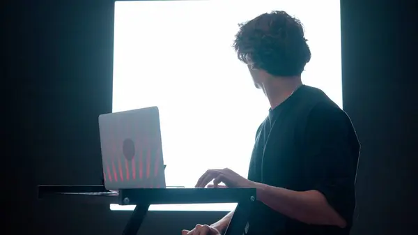 デジタルビジュアルテクノロジーコンセプト ダーククラブのデジタルウォールで ノートパソコンで働く若い男性です ラップトップでタイピングする男のシルエット 大きなデジタル画面の前にミキシングミュージック — ストック写真