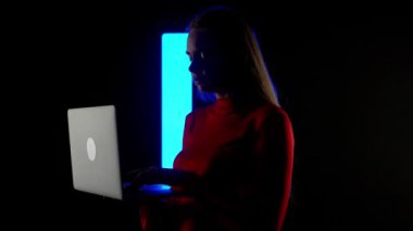 Dijital görsel teknoloji kavramı. Karanlık kulüpte dijital duvara karşı dizüstü bilgisayarı olan bir kadın silueti. Dizüstü bilgisayarda yazan, müzik çalan, dijital ekranın önünde müzik karıştıran bir kadın...