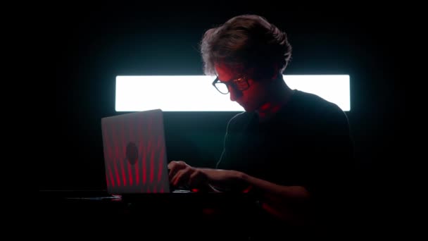 数字视觉技术概念 年轻男性在黑暗俱乐部靠着数字墙在笔记本电脑上工作 男人的轮廓坐在笔记本电脑上打字 在大的数字屏幕前游戏混音 — 图库视频影像