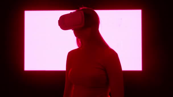 デジタルビジュアルテクノロジーコンセプト デジタルスクリーンウォールの前に立っているバーチャルリアリティグラスで女性のシルエット ビデオゲームをプレイする周りを見回すネオンシンボル — ストック動画