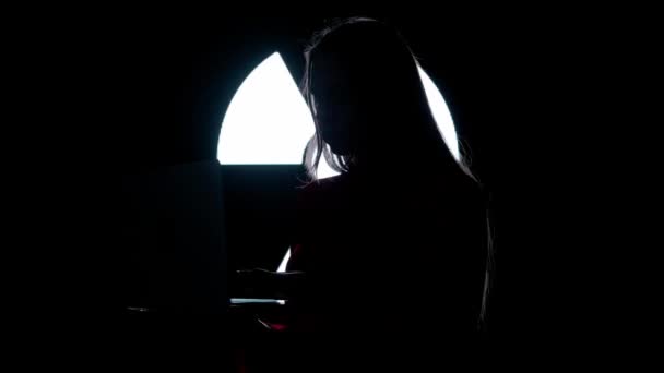 デジタルビジュアルテクノロジーコンセプト ダーククラブのデジタル壁に対してラップトップを備えた女性のシルエット ノートパソコンにタイピングする女性 デジタルスクリーンの前でミキシングミュージックをストロボシンボル — ストック動画