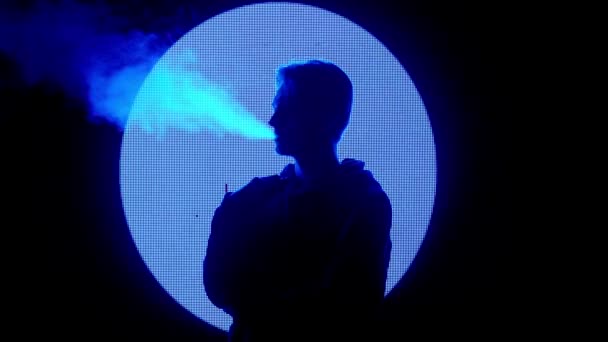 デジタルビジュアルテクノロジーコンセプト 大きなデジタル壁に対する男性 ダーククラブでネオンシンボルを刺すデジタルスクリーンウォールの前に電子タバコを喫煙する男 — ストック動画