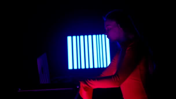デジタルビジュアルテクノロジーコンセプト ダーククラブのデジタル壁に対抗するノートパソコンを持つ若い女性 ラップトップ ゲームミキシングミュージック ストロボネオンシンボルデジタルスクリーンに座っている女性のシルエット — ストック動画