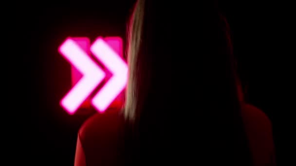 デジタルビジュアルテクノロジーコンセプト ダーククラブのデジタル壁に女性のシルエットが近づいています ネオンストロブシンボル バックショットで大きなデジタルスクリーンの背景に向かって歩く女性 — ストック動画