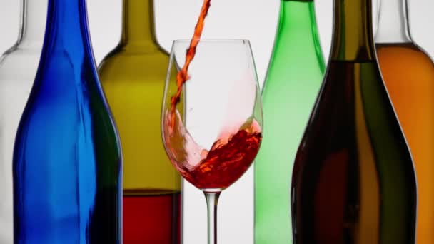 赤ワインのダイナミックな瞬間が 澄んだワイングラスに注がれています 白いバックグラウンドは 鮮やかなワインとボトルの色調に反しています クローズアップ — ストック動画