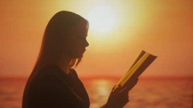 Gün batımının parlak gölgeleri karşısında kitap okuyan genç bir kadının silueti. Görüntü, doğanın güzelliğinden çekilen ilhamın özünü iletir.