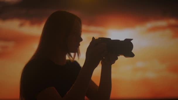 明るい日没の背景にカメラで写真を撮る若い女性のシルエット — ストック動画